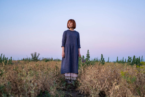 Young redhead woman with  freckles in vintage handmade dress walk in fields with flowers  - 写真・画像