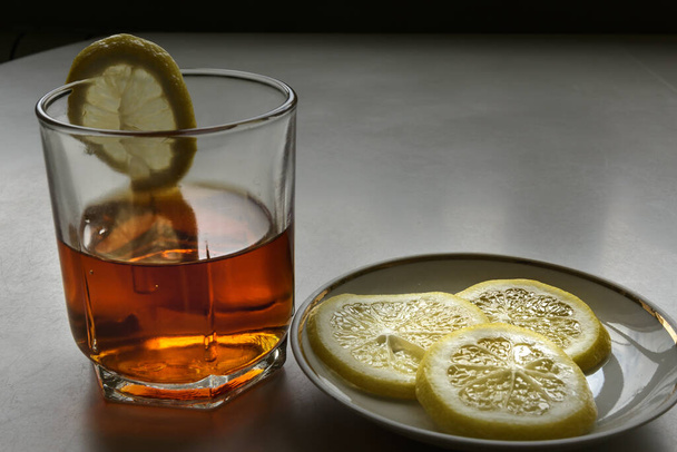 Whiskey in a crystal glass and a lemon on a porcelain dish - Photo, Image