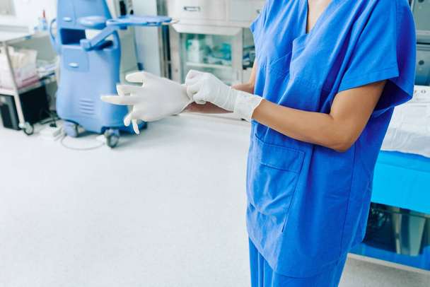 手術室で白い滅菌外科用手袋を着用する外科医の作物イメージ - 写真・画像