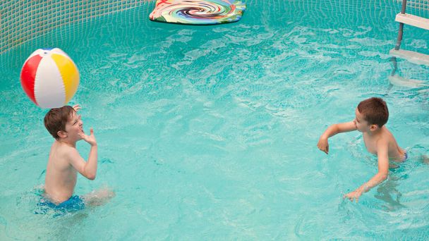 Happy kids playing in the swimming pool with ball and water mattress. Having fun in water pool outside on summer day. Leisure and swimming at holidays. Happiness and joy. - Photo, Image