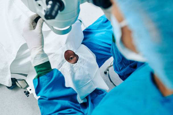 Хирургический ассистент устанавливает лазерное оборудование над пациентом и готовится к коррекции зрения - Фото, изображение