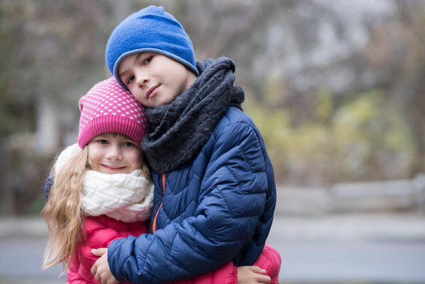 Two children boy and girl hugging each other outdoors wearing warm clothes in cold autumn or winter weather. - Фото, зображення