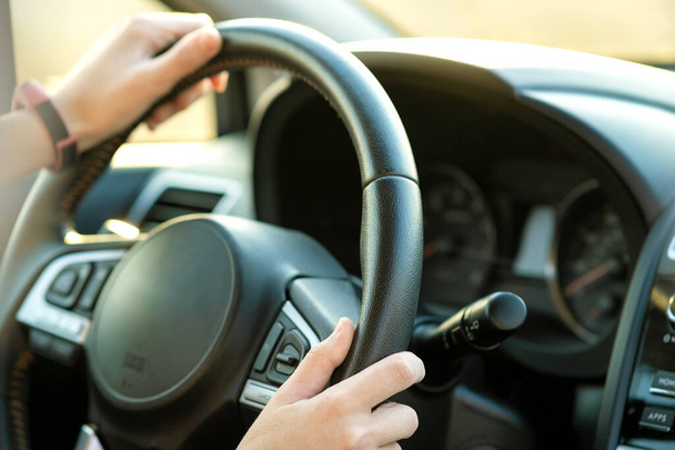 Γκρο πλαν άποψη της γυναίκας χέρια κρατώντας τιμόνι οδήγηση αυτοκινήτου στο δρόμο της πόλης την ηλιόλουστη μέρα. - Φωτογραφία, εικόνα