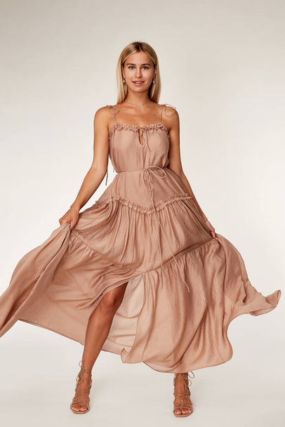 Pretty beautiful sexy elegance woman skin tan body fashion model glamor pose wear  long beige silk trend dress party summer collection makeup hair style blond success jewelry studio. - Photo, Image