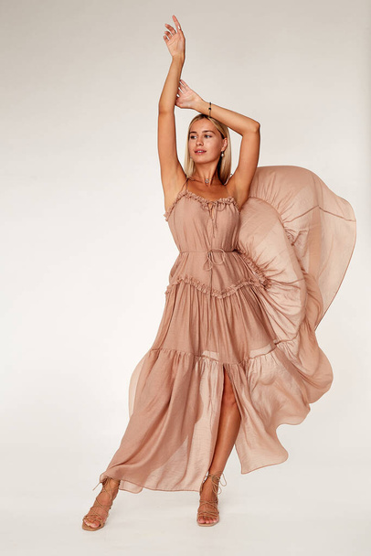 Pretty beautiful sexy elegance woman skin tan body fashion model glamor pose wear  long beige silk trend dress party summer collection makeup hair style blond success jewelry studio. - Photo, image
