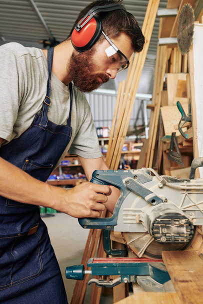 Komoly profi asztalos fülvédőben körfűrésszel vágja a fából készült deszkát - Fotó, kép