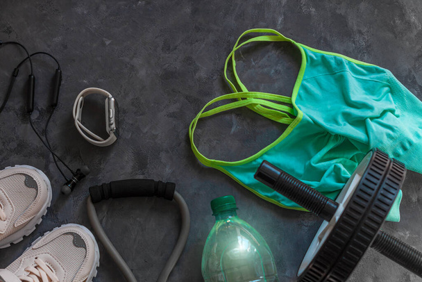 Sports lifestyle flatlay composition, trendy white sneakers, sport watch, aqua turquoise bra, headphones, fitness chest expander, ab wheel abdominal training, water bottle on grey concrete background. - Photo, Image