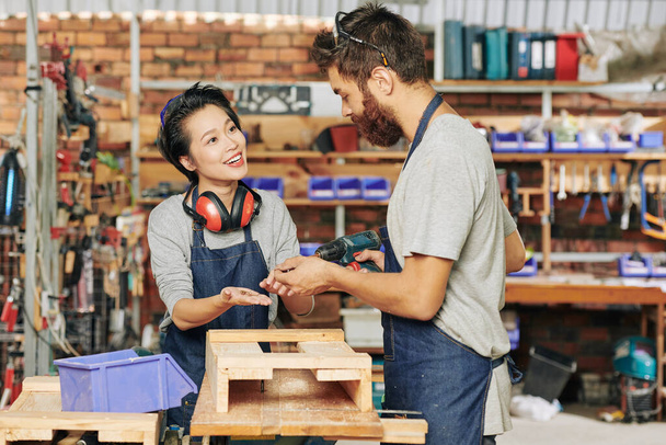 Pretty smiling female carpenter giving screws to her coworker assembling drawer - Photo, Image