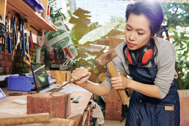 Концентрированный вьетнамский плотник при резке древесины использует стамеску и молоток - Фото, изображение