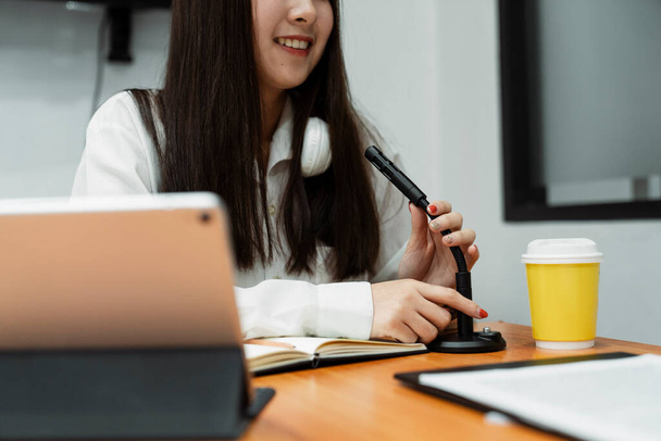 Oříznutý obrázek černé dlouhé vlasy dívka v bílé košili s bílým sluchátkem kolem krku, zatímco zkontrolovat mikrofon. - Fotografie, Obrázek