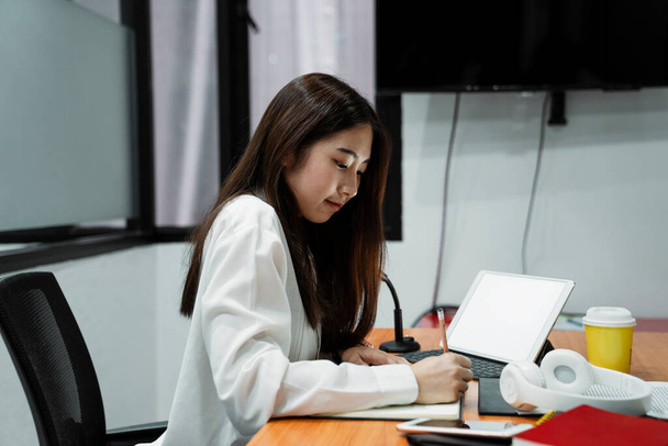 Black long hair girl in white shirt wearing take the note on her notebook while finding the information on the internet with tablet. - 写真・画像