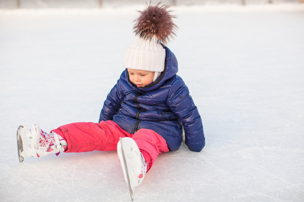 αξιολάτρευτο κοριτσάκι που κάθεται στον πάγο με πατίνια μετά την πτώση - Φωτογραφία, εικόνα