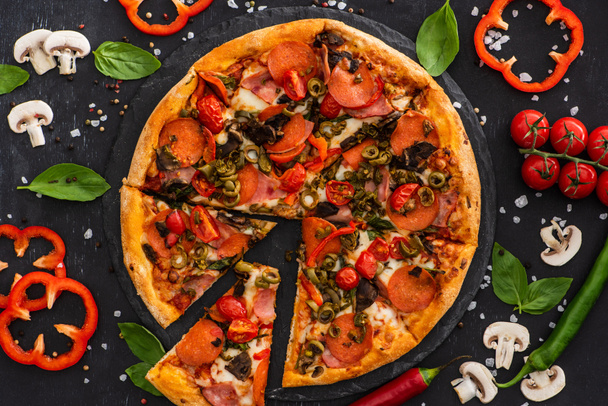 top view ízletes olasz pizza zöldségekkel és szalámi fekete háttér - Fotó, kép