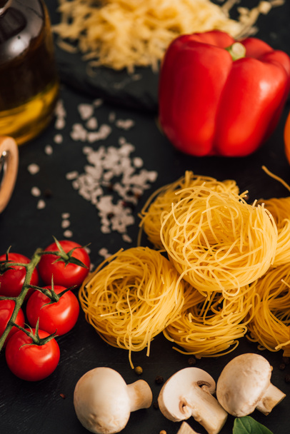 selective focus of raw Italian Capellini with vegetables and salt on black background - Foto, afbeelding
