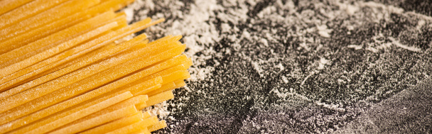 close up view of raw spaghetti and flour on black background, panoramic shot - Zdjęcie, obraz