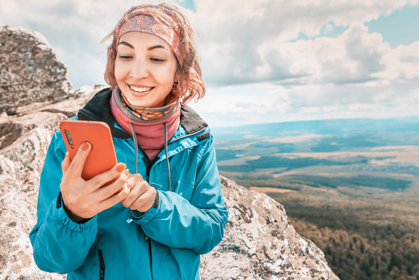 Mujer asiática en la cima de una montaña se conecta a un navegador GPS y una aplicación en su teléfono para chatear con amigos. Comunicación celular e Internet móvil en una caminata turística - Foto, imagen