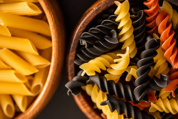 κοντινή προβολή πολύχρωμων ακατέργαστων ιταλικών ζυμαρικών σε ξύλινα μπολ - Φωτογραφία, εικόνα