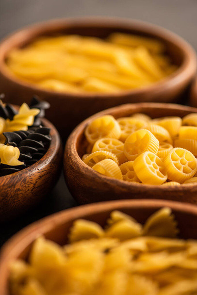 selective focus of raw fusilli and rotelle pasta in wooden bowls - Фото, зображення
