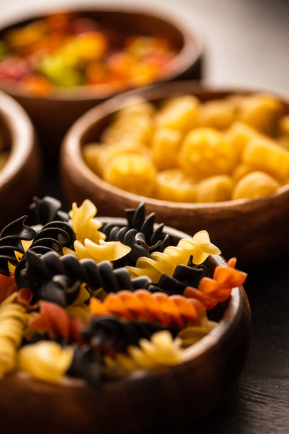 selective focus of colorful raw fusilli pasta in wooden bowl - 写真・画像