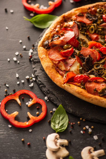 selective focus of delicious Italian pizza with salami near vegetables on black background - Photo, Image