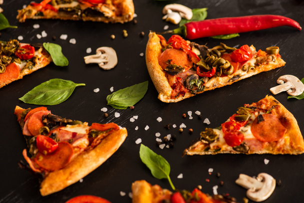 szelektív fókusz ízletes olasz pizza szeletek szalámi mellett zöldségek fekete alapon - Fotó, kép