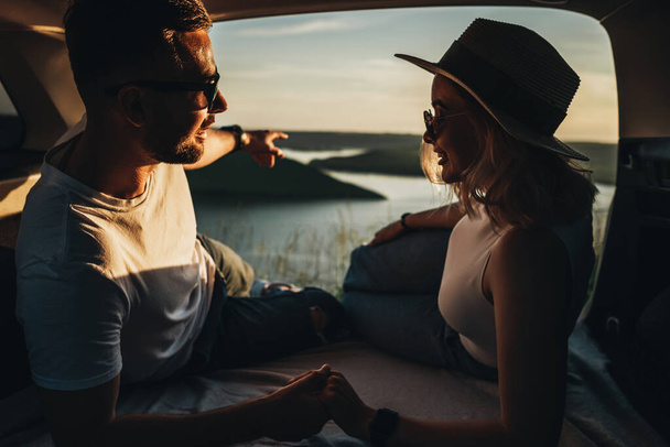 Mann und Frau entspannen sich im Kofferraum des Autos und genießen Wochenend-Roadtrip, Reise- und Abenteuerkonzept - Foto, Bild