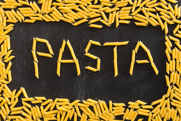 bovenaanzicht van pasta woord gemaakt van rauwe penne op zwarte achtergrond - Foto, afbeelding