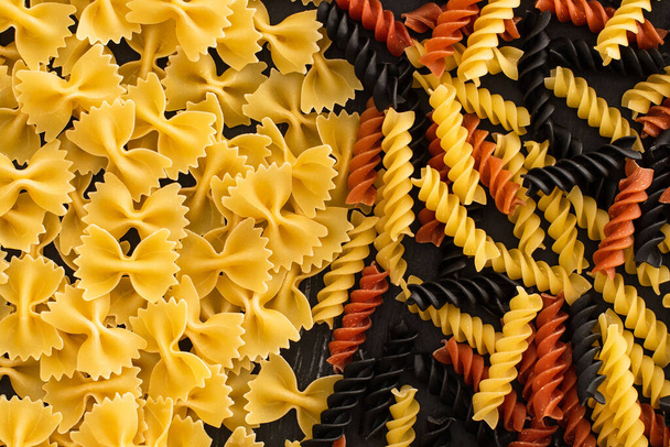 bovenaanzicht van rauwe kleurrijke fusilli en farfalle pasta - Foto, afbeelding