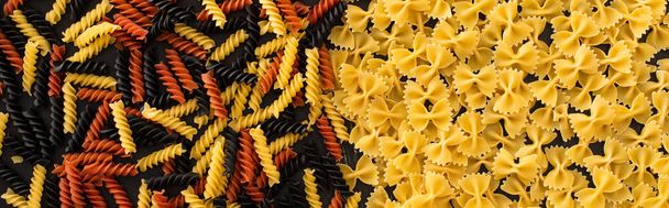 bovenaanzicht van rauwe kleurrijke fusilli en farfalle pasta, panoramisch schot - Foto, afbeelding