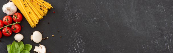 πάνω όψη της ακατέργαστης ιταλικής σπαγγέτι με λαχανικά και μπαχαρικά σε μαύρο φόντο, πανοραμική λήψη - Φωτογραφία, εικόνα