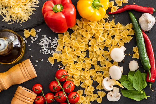 top view of raw Italian farfalle with vegetables and seasoning on black background - 写真・画像