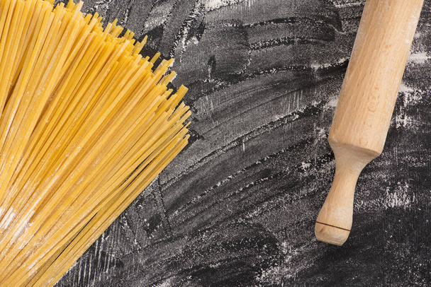 top view of raw spaghetti near rolling pin on flour on black background - Фото, зображення