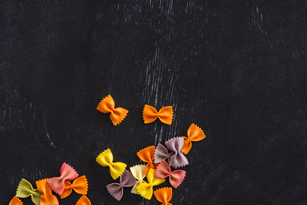 top view of colorful raw farfalle pasta on black wooden background - Photo, Image