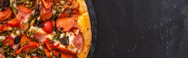 вид сверху на вкусную итальянскую пиццу с салями на черном деревянном фоне, панорамный снимок - Фото, изображение