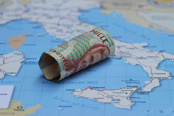 Walcowane pieniądze banknotów tysiąc lirów Włochy umieścić na mapie Włoch. Pojęcie finansowania, waluty lub podróży. - Zdjęcie, obraz