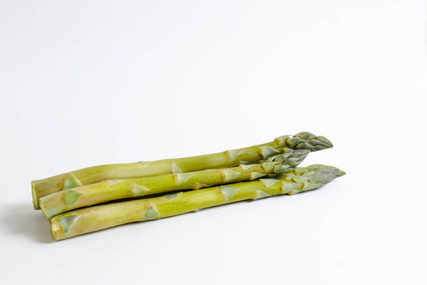 Bunch of raw asparagus stems isolated on white. Edible Asparagus Officinalis sprouts laid on paper textured background. Close up, copy space, top view, flat lay. - 写真・画像