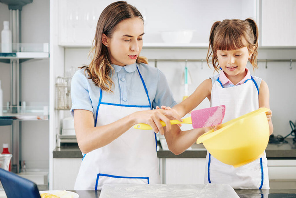 Petite fille en tablier blanc aidant mère avec la fabrication de pâte à biscuits et la cuisson dans la cuisine - Photo, image