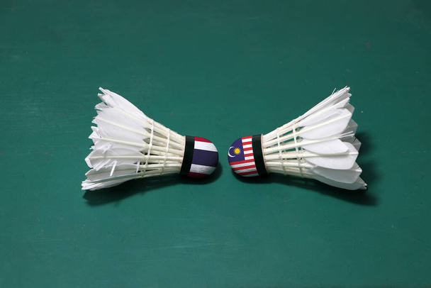 Dwa używane wahadłowce na zielonym piętrze sądu w Badminton z obiema głowami. Jedna głowa malowana tajską flagą i jedna głowa malowana flagą Malezji, koncepcja konkursu badmintona. - Zdjęcie, obraz