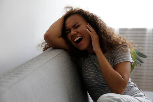 Portrait of young beautiful black woman experiencing excruciating migraine grabbing her head. Female expressing physical and emotional pain. Sad girl in her room. Background, copy space. - Foto, Bild