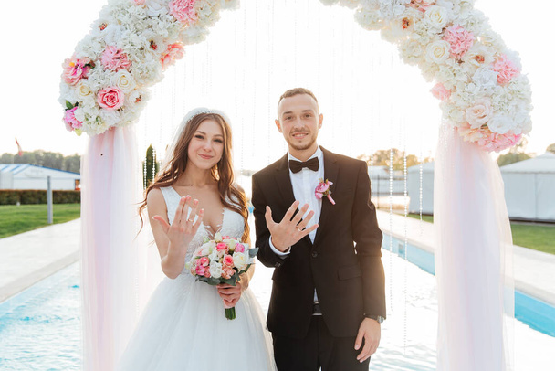 Luxuriös schönes Paar, der Bräutigam im schwarzen Anzug und die Braut im weißen Hochzeitskleid, tauschten bei einer Ausstiegszeremonie mit einem Bogen die Ringe, Hochzeit im Herbst - Foto, Bild