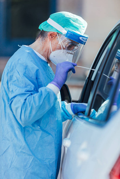 Personel medyczny noszący ŚOI, wykonujący PCR z wymazem w dłoni, na pacjencie w samochodzie w celu wykrycia, czy jest zakażony COVID-19 - Zdjęcie, obraz