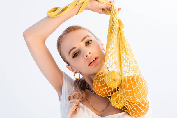 fashionable woman posing with citrus fruits in string bag isolated on white - Foto, Imagem