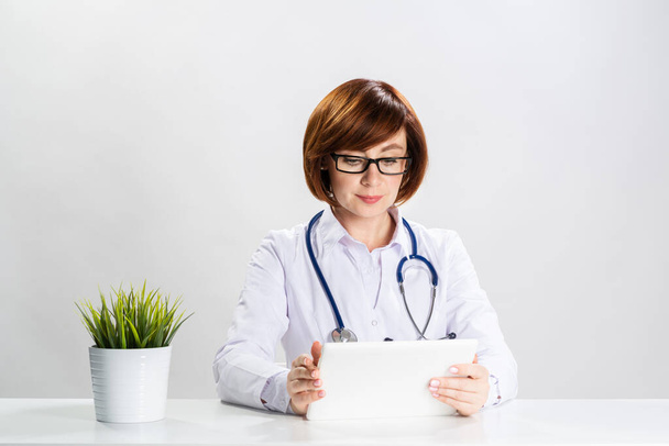Redhead doctor using tablet computer in office - Photo, image