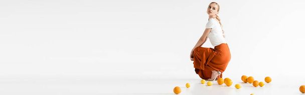 白地に柑橘系の果実の近くにポーズをとるエレガントなブロンドの女性の側面図パノラマショット - 写真・画像