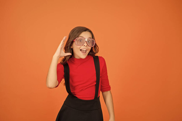 i cant hear you. pretty and stylish child. happy small girl school uniform. party glasses for fun. kid fashion concept. Staying focused with glasses. cool looking pupil orange background - Fotó, kép