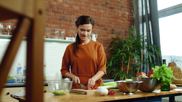 Γυναίκα τεμαχίζει ντομάτα σε ξύλο κοπής. Κορίτσι ρίχνουν λαχανικά σε μπολ σαλάτα. - Φωτογραφία, εικόνα