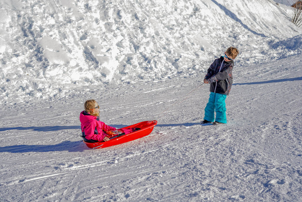 Bruder zieht seine Schwester Kinder Rodelschlitten Schnee. Kleine Mädchen und Jungen genießen die Schlittenfahrt. Kinderrodeln. Kinder spielen draußen im Schnee. - Foto, Bild