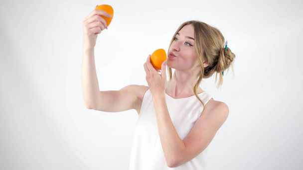 A young girl with oranges in her hands on a white background,a woman in a white dress - Фото, изображение