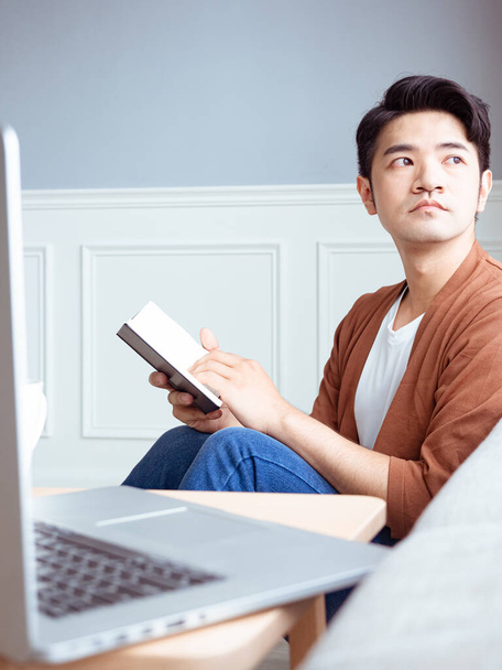 Jeune homme asiatique lisant un livre tout en se relaxant à la maison - Photo, image