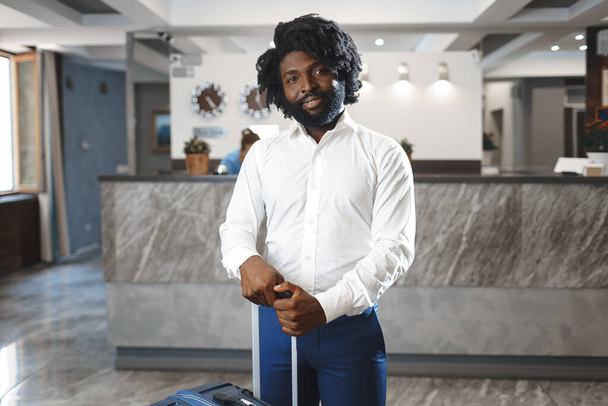 Black businessman with packed luggage standing in hotel lobby - Foto, Bild